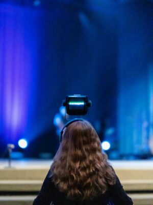 Female camera operator records live concert, capturing vibrant stage performance.