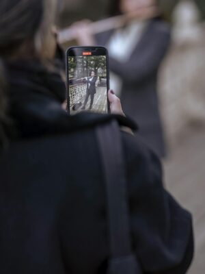 Woman recording a musician playing the flute outdoors, captured on a smartphone.