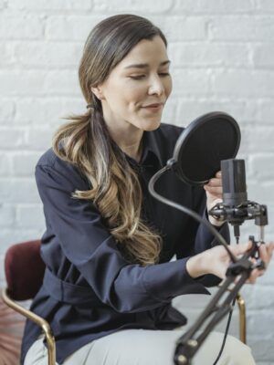 Woman recording a podcast in a modern studio with a microphone and pop filter, showcasing a professional setup.