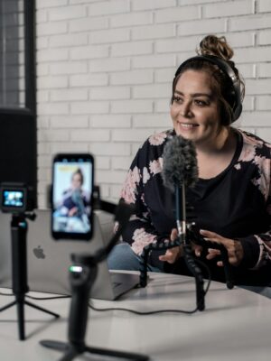 Woman recording video podcast with microphone and camera setup in modern studio.